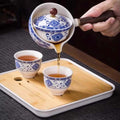 Porcelain Gongfu 360-degree rotation tea pot pouring tea into matching blue and white porcelain cups on bamboo tray