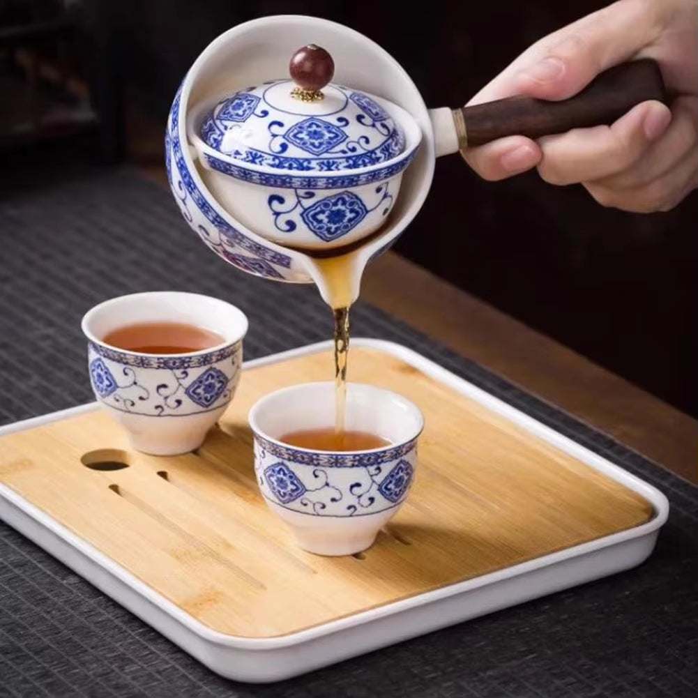 Porcelain Gongfu 360-degree rotation tea pot pouring tea into matching blue and white porcelain cups on bamboo tray